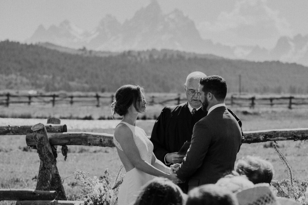 couple holds hands in at wedding ceremony with a viw of the Tetons in the backdrop at Diamond Cross Ranch