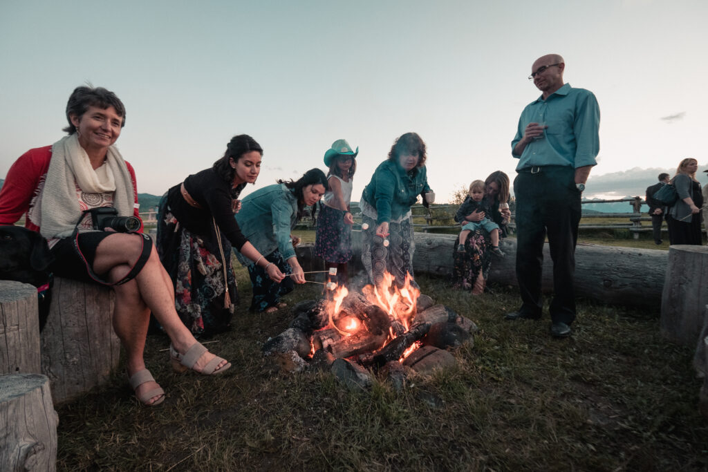 wedding guests make smores aroun a campfire at sunset at the Diamond Cross Ranch in Jackson Hole, Wyoming